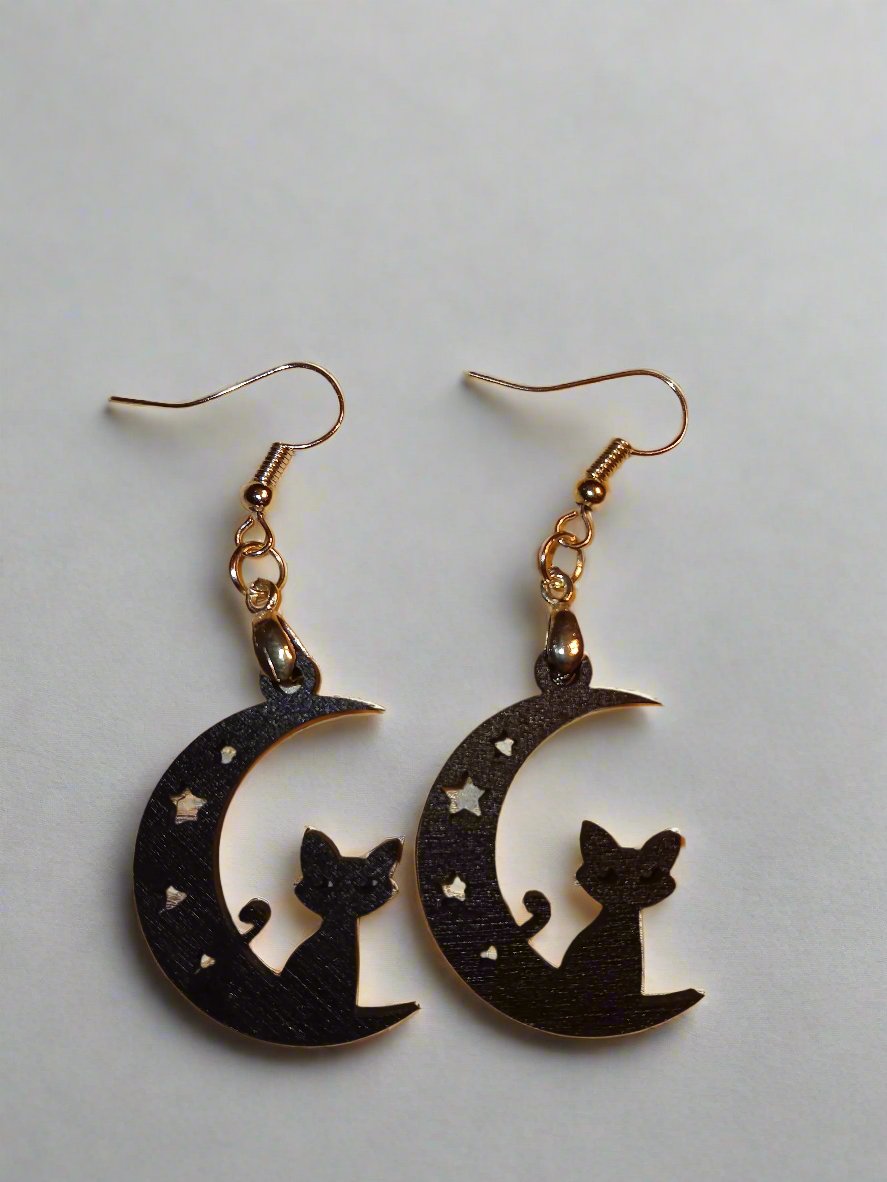 A pair of Spooky Earrings featuring black cat silhouettes sitting on crescent moons with tiny star cutouts.