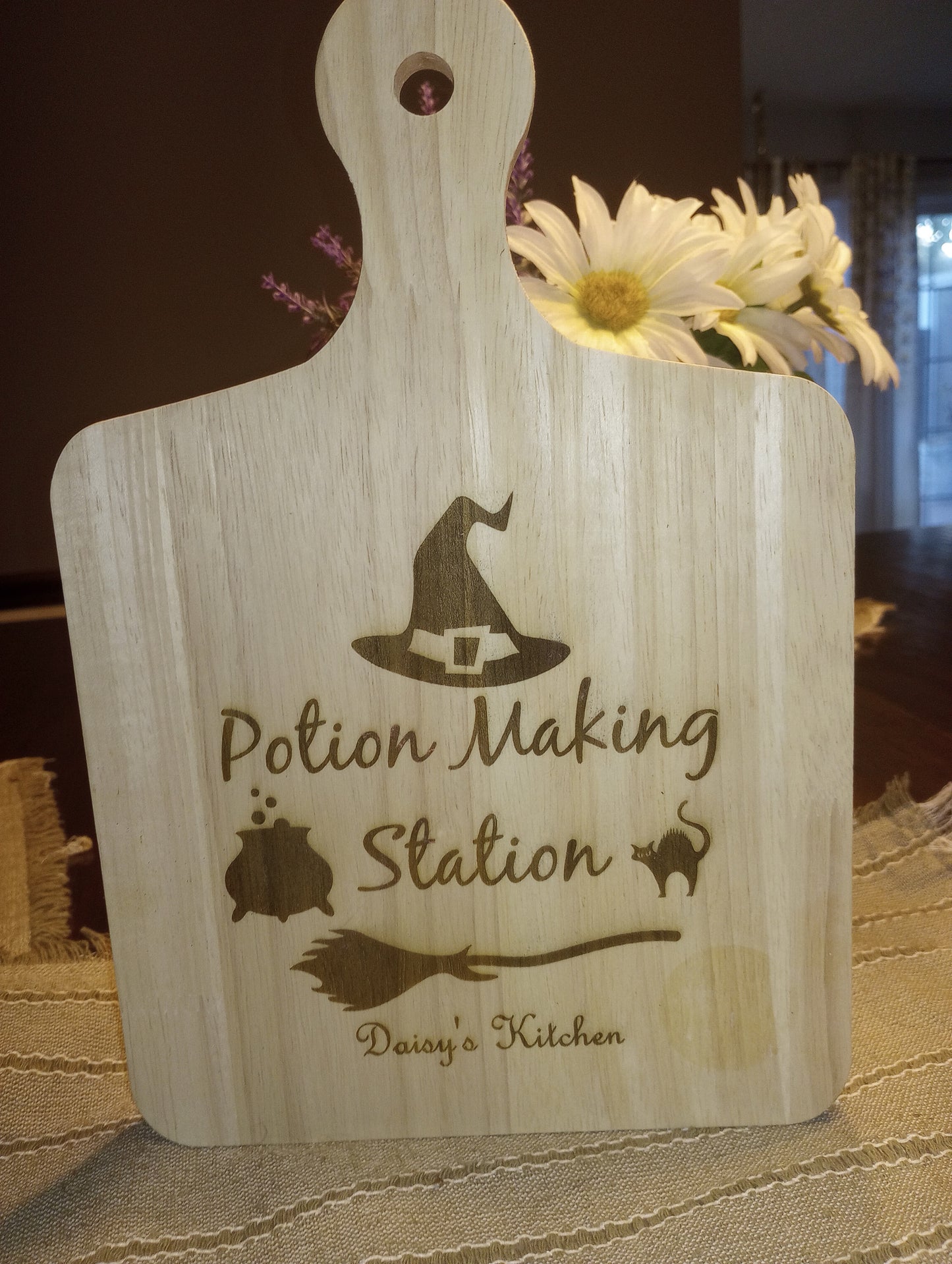 Wooden board with a witch hat, cauldron, cat, and broomstick engraved. Text reads: "Potion Making Station" - [Personalized Name]'s Kitchen.