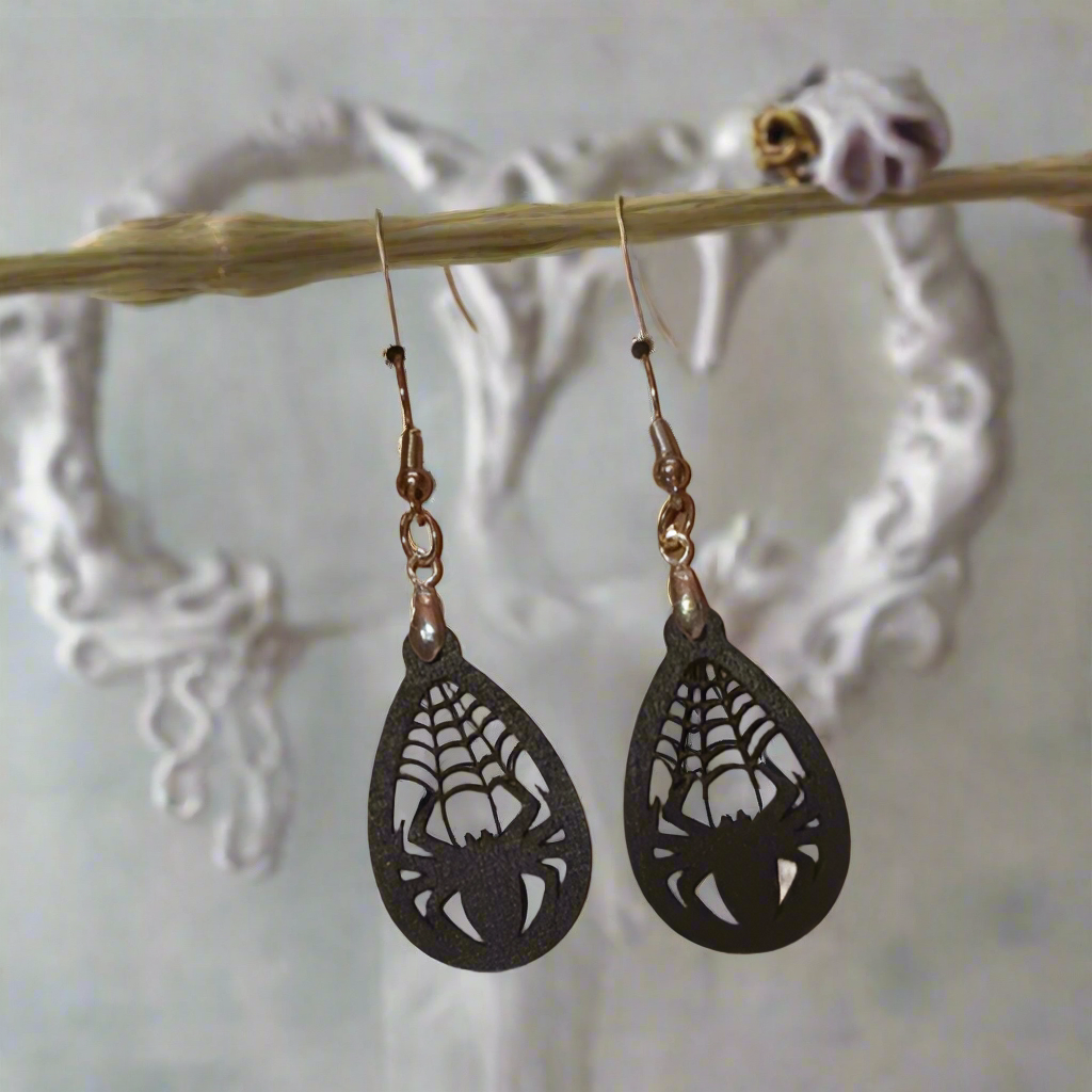 A pair of spider web-themed earrings hanging from a branch, perfect for Halloween or spooky occasions.