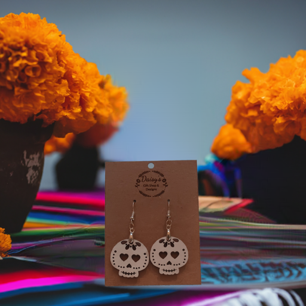 Spooky Earrings product image: Pair of white skull-shaped earrings with heart eyes on a brown card, surrounded by bright orange marigolds.