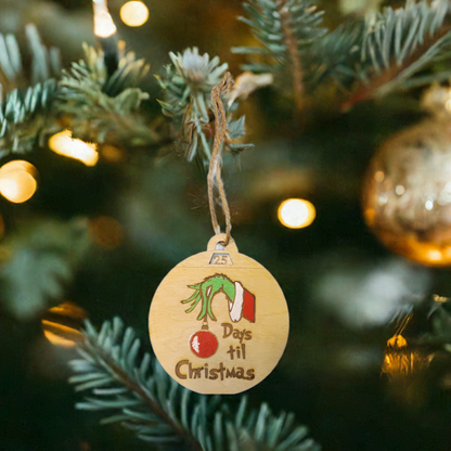 A wooden Christmas ornament hanging on a tree branch, displaying "25 Days 'til Christmas" with festive decorations.