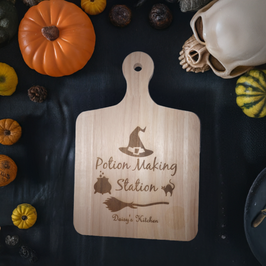 Wooden board with "Potion Making Station" engraved, surrounded by pumpkins and Halloween decor. Customizable text: "Daisy's Kitchen."