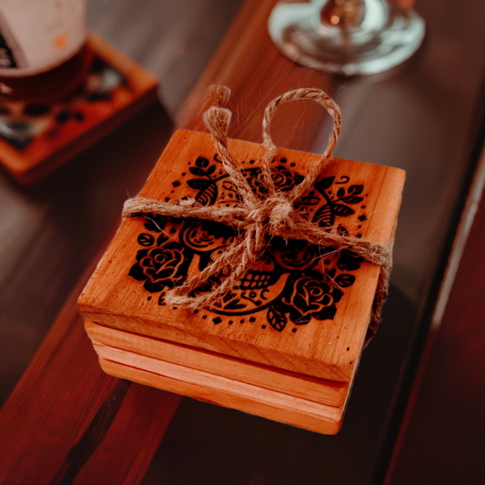 A set of wooden coasters with skull and rose engravings, tied together with twine, displayed on a table.