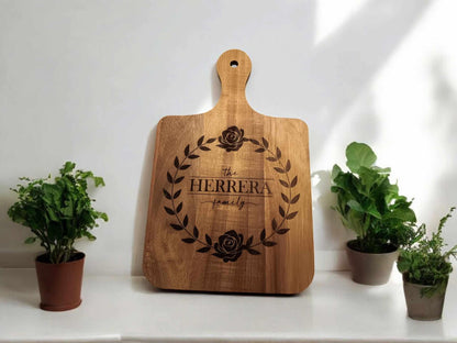 16x10 personalized cutting board with "Herrera Family" and floral wreath engraving, displayed between potted plants.